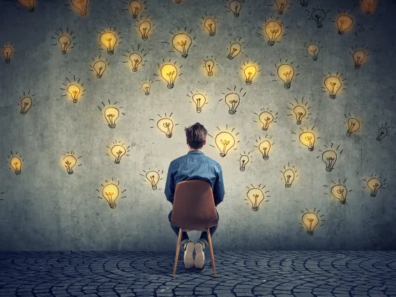 man sitting in chair facing wall painted with light bulbs