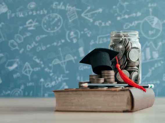 graduation cap and jar of coins sitting atop a book