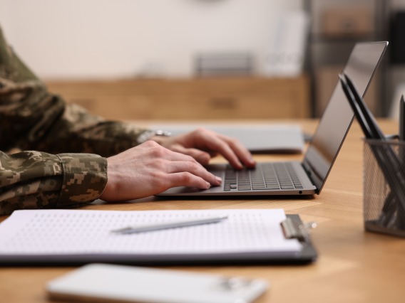 person in military uniform typing on laptop